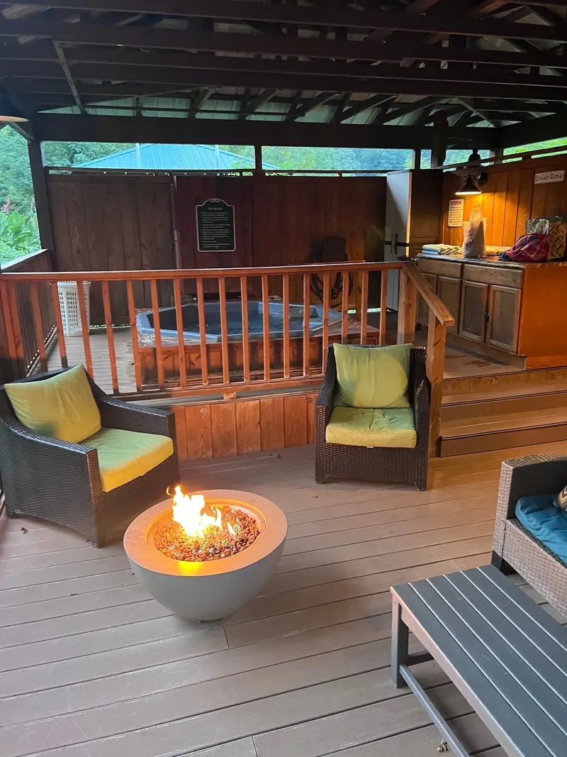 Roofed bath enclosure with wooden railings, cushioned chairs and a fire bowl at Hot Springs Resort