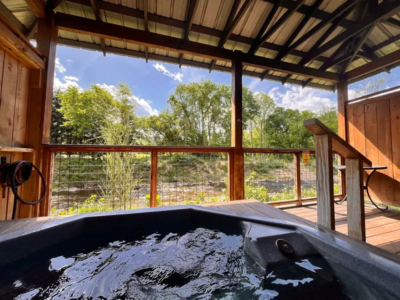Dark soaking bath beneath a timber roof beside a wooded waterway at Hot Springs Resort
