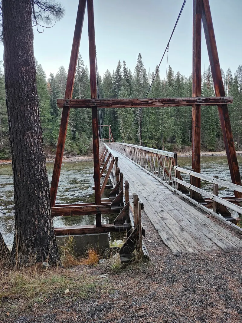Wooden suspension bridge over a forest-lined river in the Jerry Johnson collection; historical approach context, not current bridge-condition confirmation