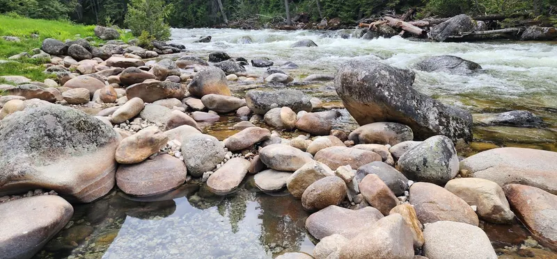 Rounded boulders, shallow foreground water and flowing water behind in the Jerry Johnson collection; scenery, not an identified safe soaking entry