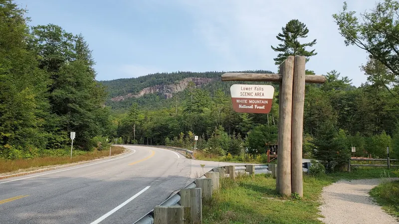 Lower Falls Scenic Area entrance sign beside the Kancamagus Highway and wooded cliffs