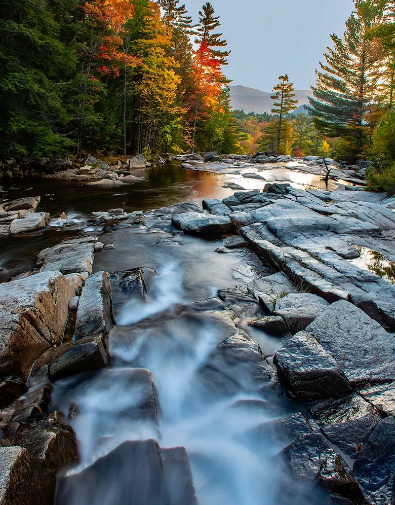 Swift River flowing over broad rock ledges beneath autumn-colored trees in the Lower Falls collection