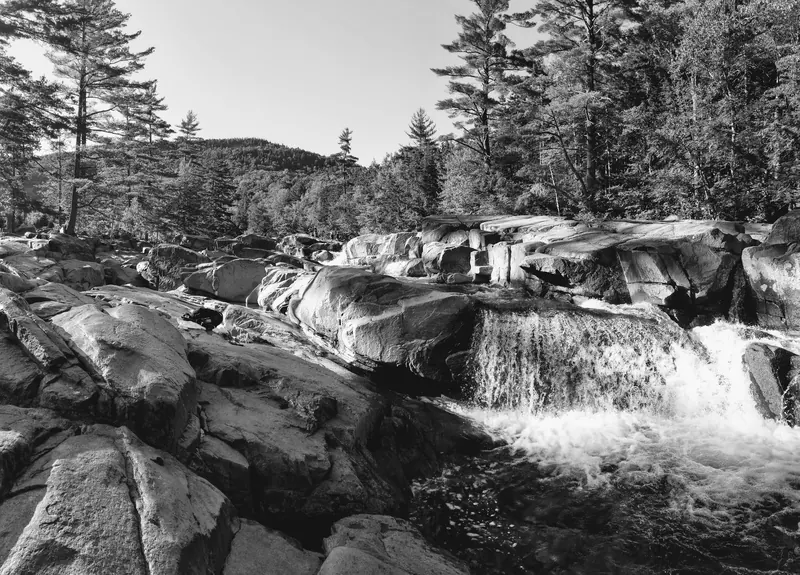 Black-and-white view of a low cascade flowing among broad rocky ledges at Lower Falls