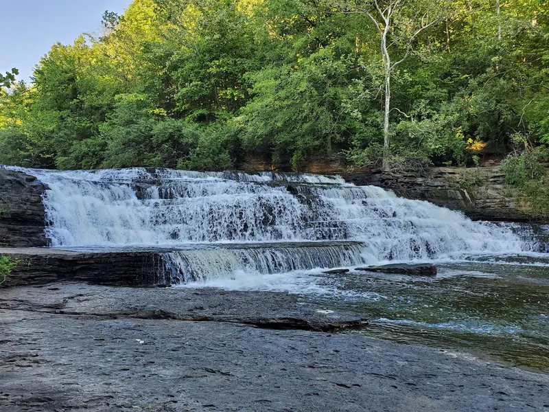 Water cascading over tiered rock below Kinkaid Lake Spillway, with a wooded bank behind