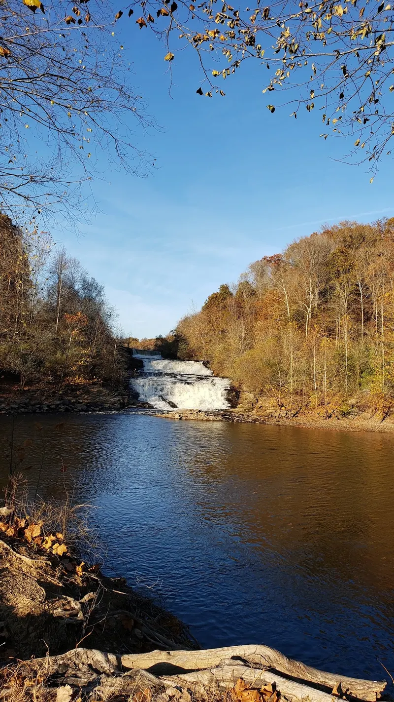 Historical autumn view of the pool below Kinkaid Lake Spillway framed by trees and a fallen log