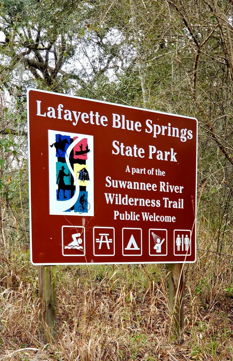 Lafayette Blue Springs State Park entrance sign beside woodland; historical signage does not confirm current camping availability