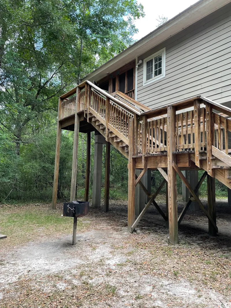 Historical exterior view of a raised cabin, wooden stairs and ground-level grill at Lafayette Blue Springs State Park; not a water-entry route
