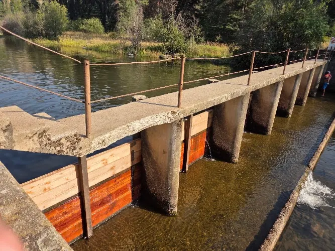 Concrete dam with wooden gates and rope railing beside river water in the Laird Park collection