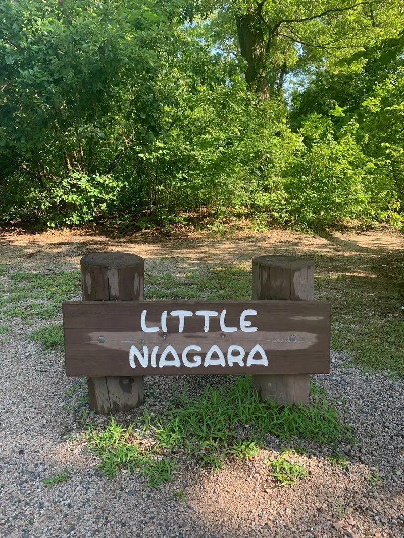 Wooden Little Niagara sign beside a gravel path and woodland