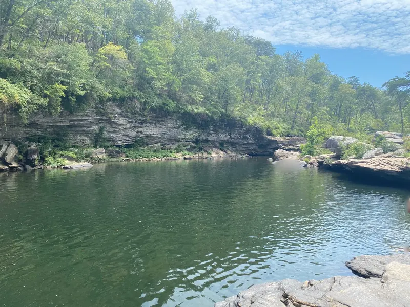 Broad river pool below layered sandstone banks in the Little River Canyon collection, with visitor regions blurred; exact pool and entry unverified
