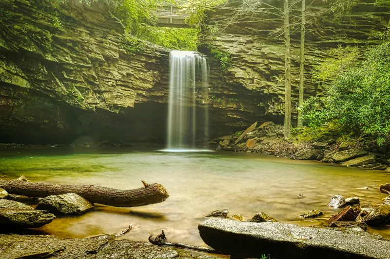 Little Stony waterfall below a wooden footbridge, framed by layered rock walls and green foliage