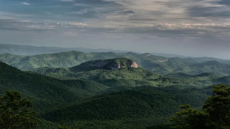 Looking Glass Rock's exposed face above forested mountain ridges in the NPS overlook photograph