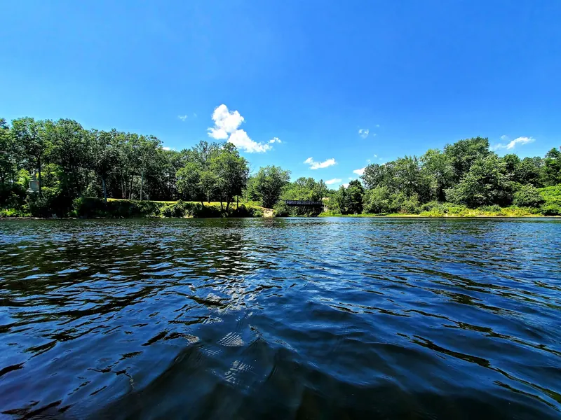 Merrimack River view toward a wooded bank and small bridge, not a verified swimming entry