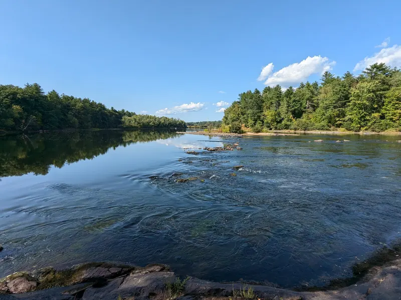 Exposed rocks and moving water between wooded Merrimack River banks in a historical photo