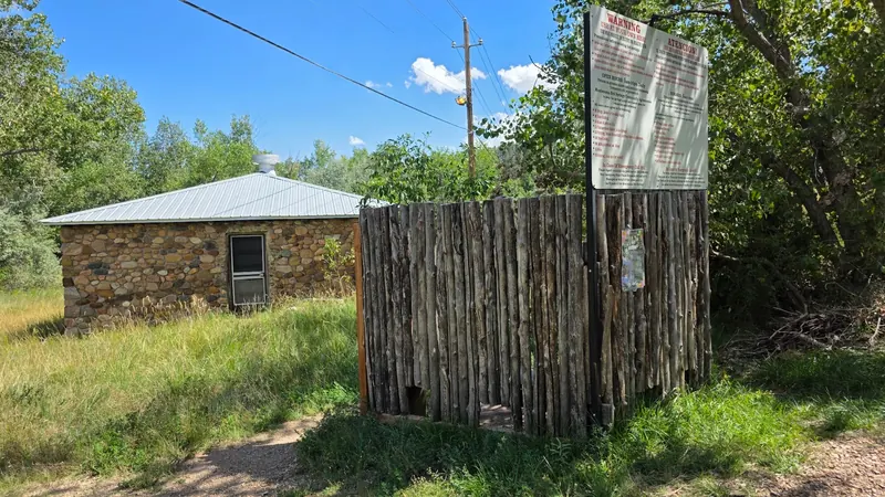 Wooden entrance gate with a historical bilingual warning sign in the Montezuma Hot Springs collection; consult current community agreements