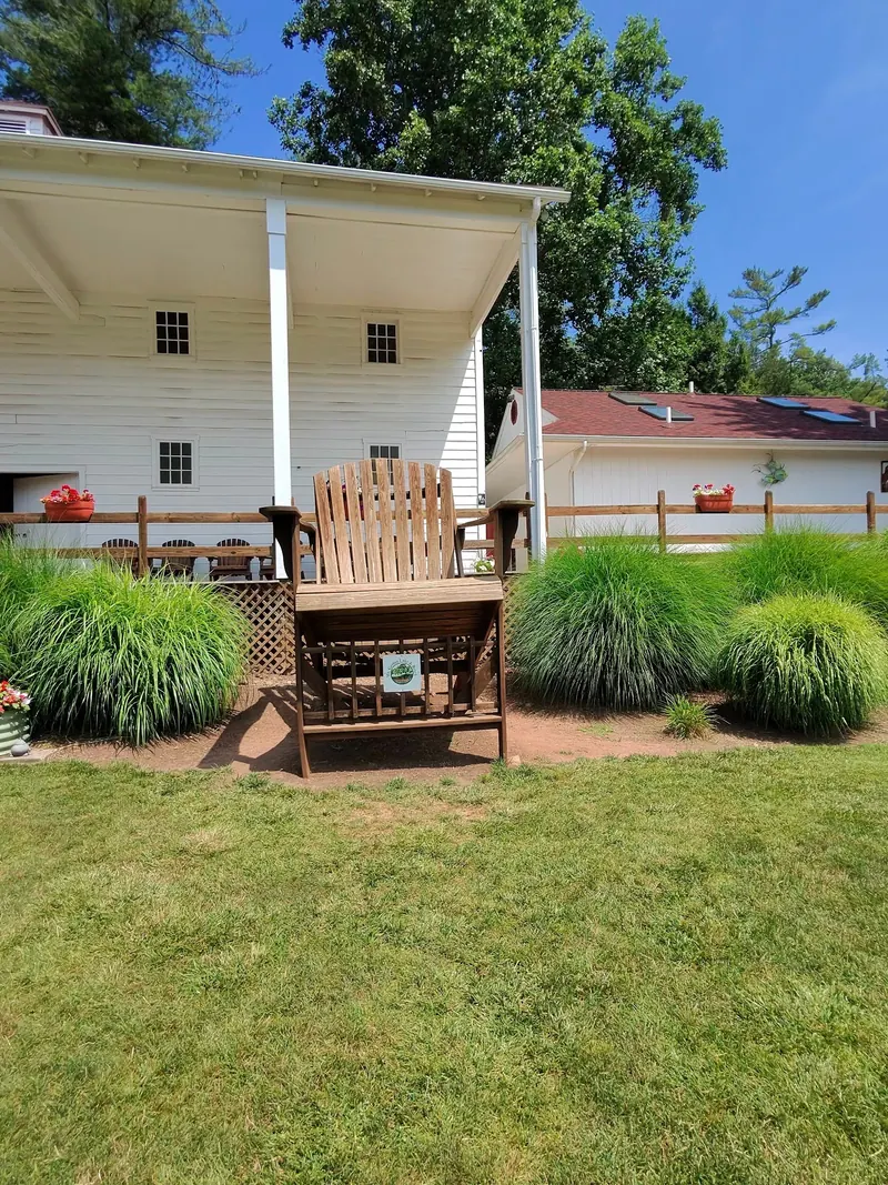 Empty oversized wooden chair beside white buildings and ornamental grasses at Mt. Gretna Lake and Beach