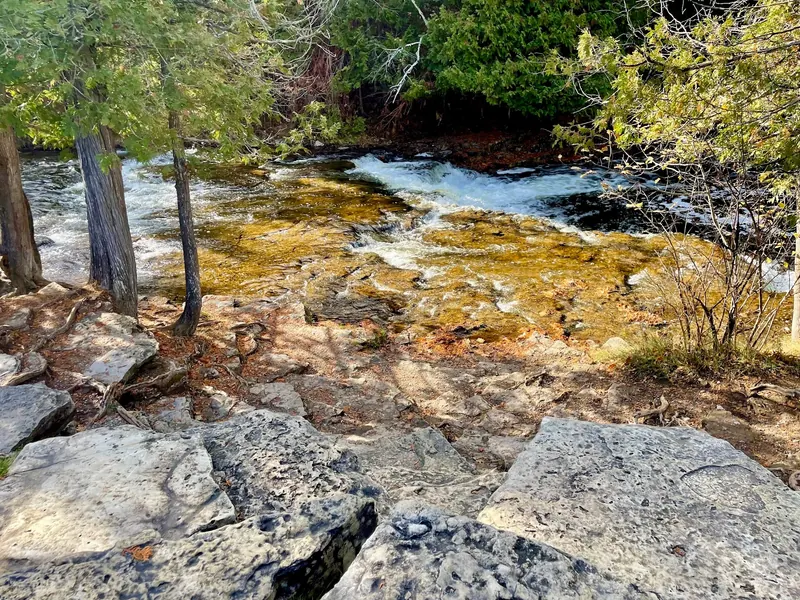 Rocky riverbank and water flowing over low ledges at Ocqueoc Falls