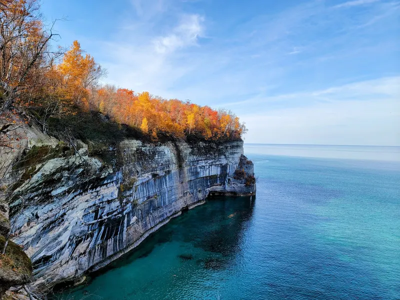 Autumn trees above layered lakeside cliffs in the Pictured Rocks collection