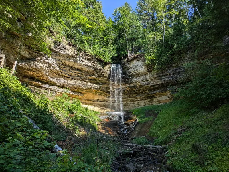 Woodland waterfall dropping into a layered rock amphitheater in the Pictured Rocks collection