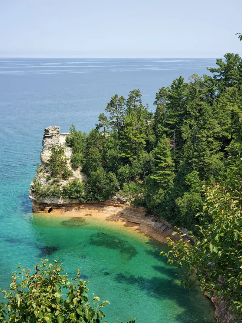 Wooded sandstone headland above blue and green Lake Superior water in the Pictured Rocks collection
