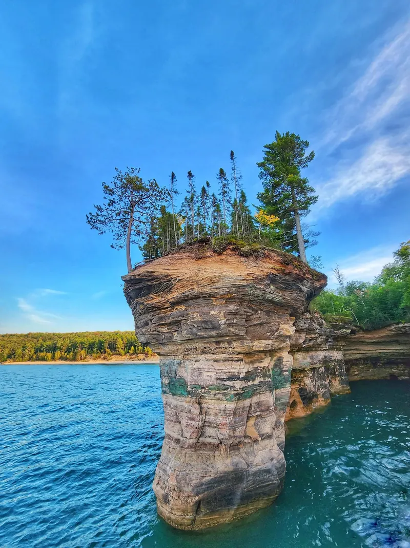 Tree-topped sandstone pillar rising from lake water in the Pictured Rocks collection