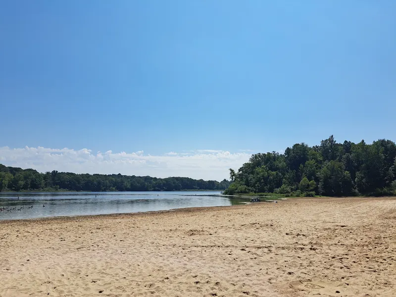Sandy swimming beach beside Punderson Lake with a wooded shoreline