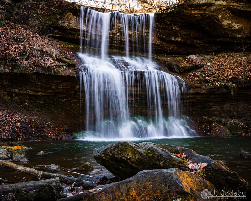 Tiered Quaker Falls waterfall among rock and autumn leaves, with the original photographer mark retained