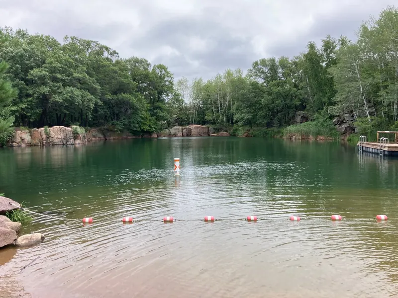Buoy-marked swimming area with a wooden platform and wooded quarry walls at Quarry Park, Minnesota