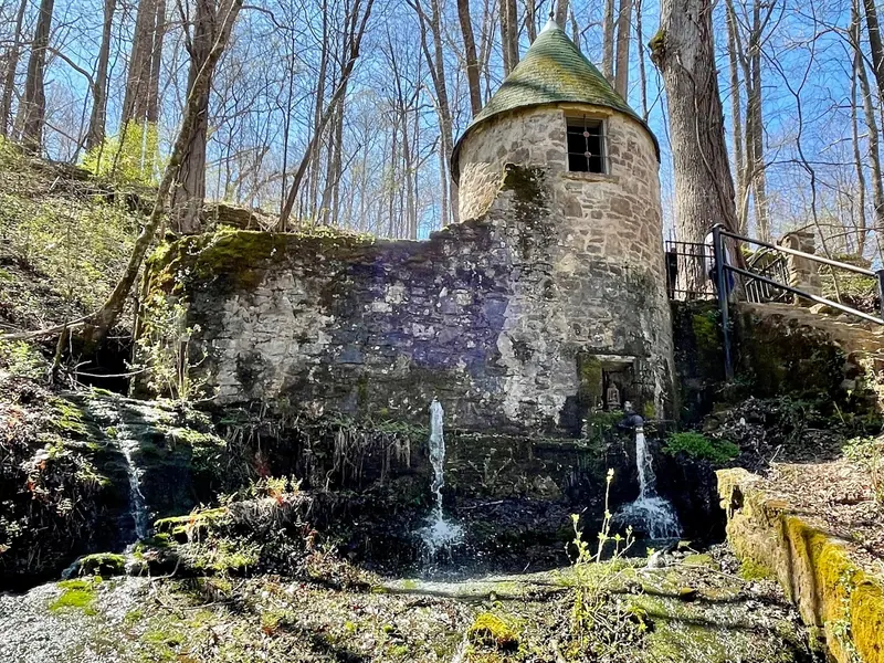 A round stone building with a conical roof and water outlets beside a wooded slope at Rock Island State Park