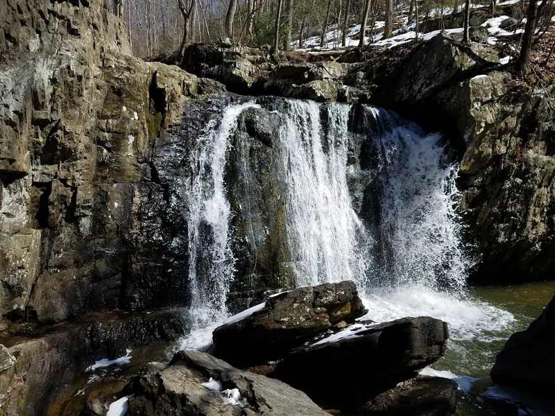 Waterfall flowing between rock walls at Rocks State Park with snow on nearby ledges