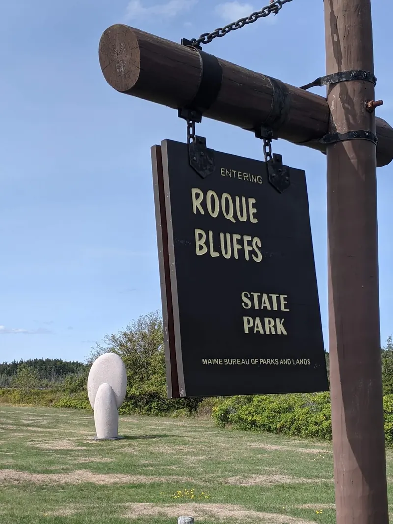 Wooden sign naming Roque Bluffs State Park above a grassy lawn; historical park identity, not today's opening status