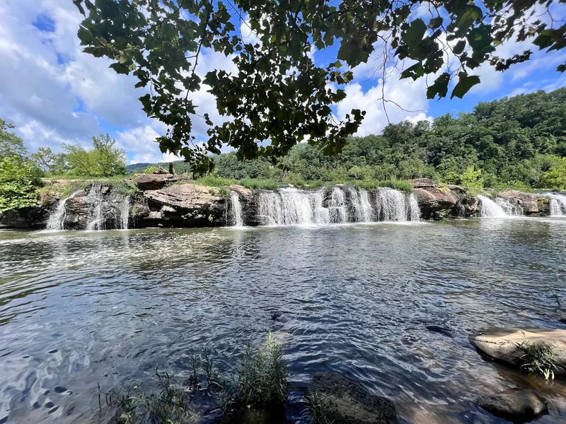 Water flowing over broad rock ledges at Sandstone Falls beneath overhanging leaves