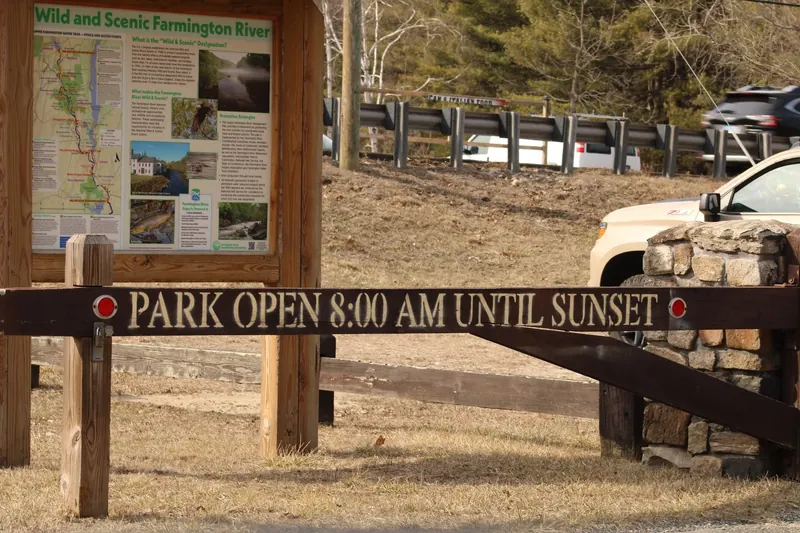 Satan's Kingdom gate displaying daytime park hours beside a Farmington River interpretive panel