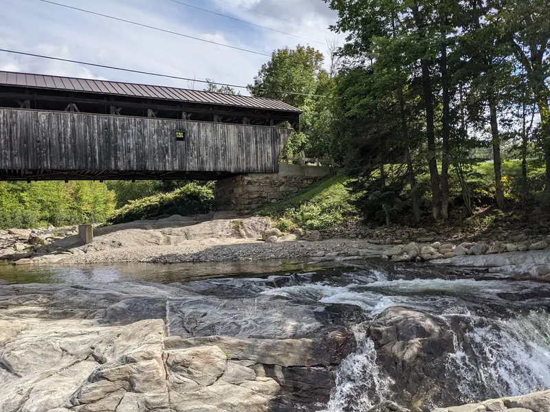 Side of Swiftwater Covered Bridge above exposed rock and flowing river water