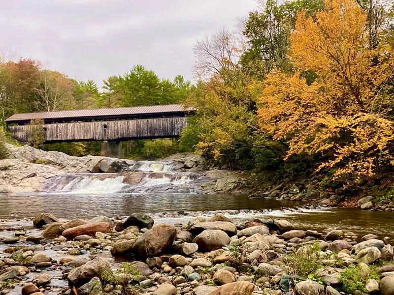 Swiftwater Covered Bridge above rocky river cascades and autumn trees in Bath