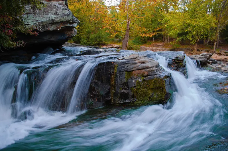 Water cascading over layered rock beside autumn trees at Turkey Creek Nature Preserve