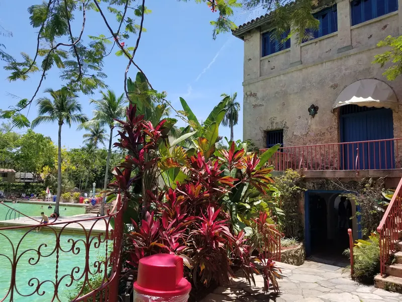 Historical Venetian Pool tower with blue shutters, red railings and tropical landscaping beside the pool; not a verified accessible entrance