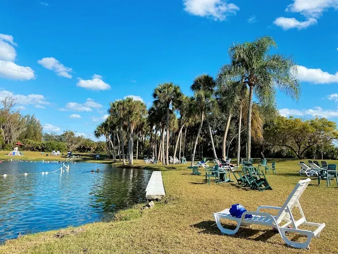 Palm-lined shoreline and lawn chairs beside Warm Mineral Springs in a historical park photograph; not current seating or facility availability