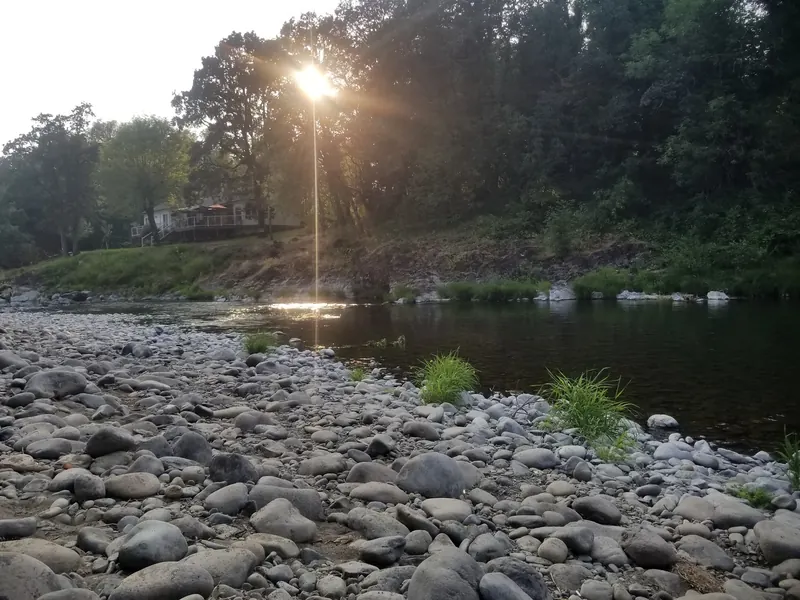 Rounded stones along the Washougal River at Sandy Swimming Hole, with evening light across the water; shoreline scenery, not a current conditions report