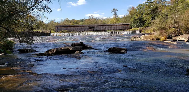 Historical rocky river shoals downstream of Watson Mill Bridge surrounded by autumn woodland; not a verified swimming-entry location