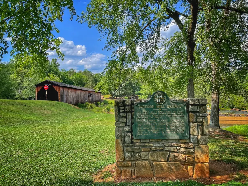 Watson Mill Bridge historical marker on a stone base with the covered bridge behind it; historical park context