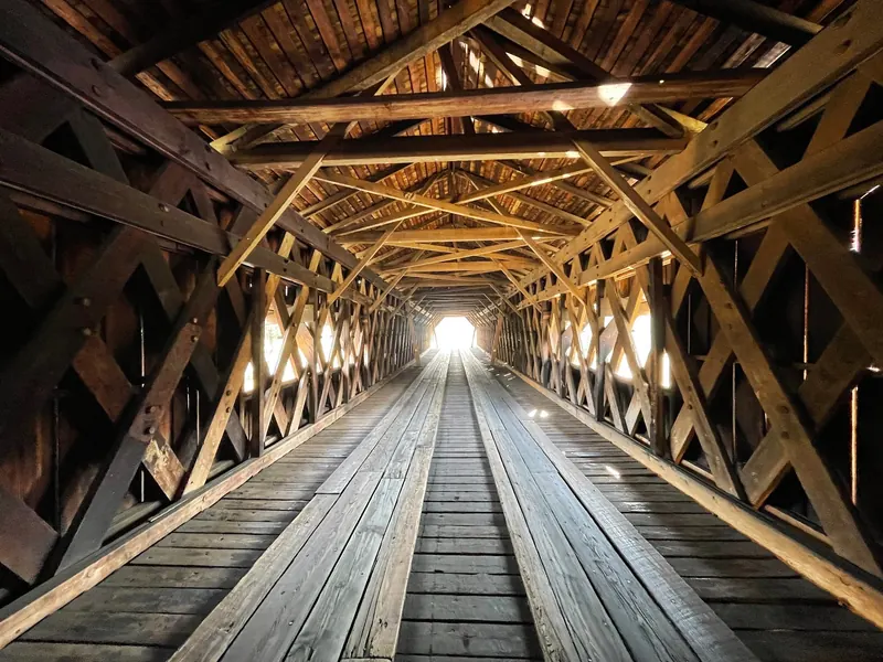 Historical timber lattice supports and plank roadway inside Watson Mill covered bridge; not confirmation of current crossing access