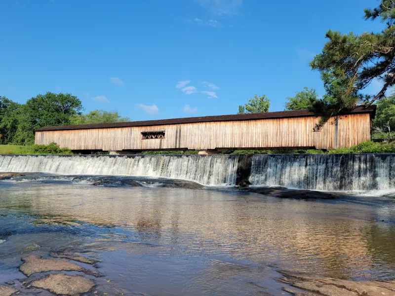 Historical Watson Mill covered bridge above the river spillway and exposed shoal rocks; not current river conditions
