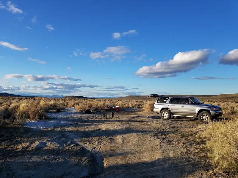 Picnic table with visitor gear and a parked SUV in open desert terrain from the Willow Creek Hot Springs collection; historical camping context