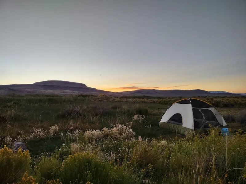 Tent among desert grasses with a flat-topped hill beyond in a historical Willow Creek camping-area photo
