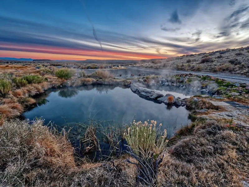 Steam rising from divided Willow Creek Hot Springs pools beneath a colorful desert sunset