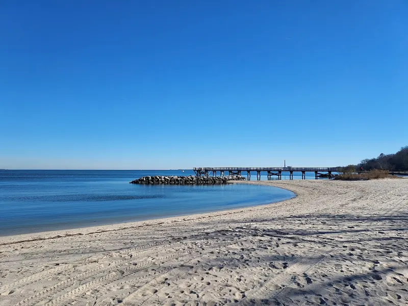 Sandy shoreline curving toward a rock breakwater and pier at Yorktown Beach