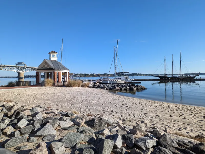 Sandy Yorktown shoreline beside a brick pavilion and moored sailboats, shown as waterfront context rather than permission to swim near docks