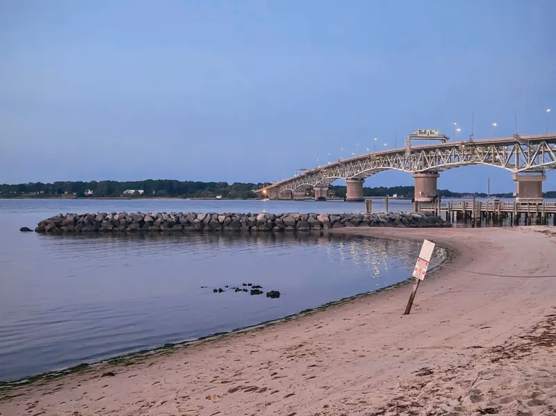 Yorktown Beach shoreline at dusk with a bridge and rock breakwater across the view